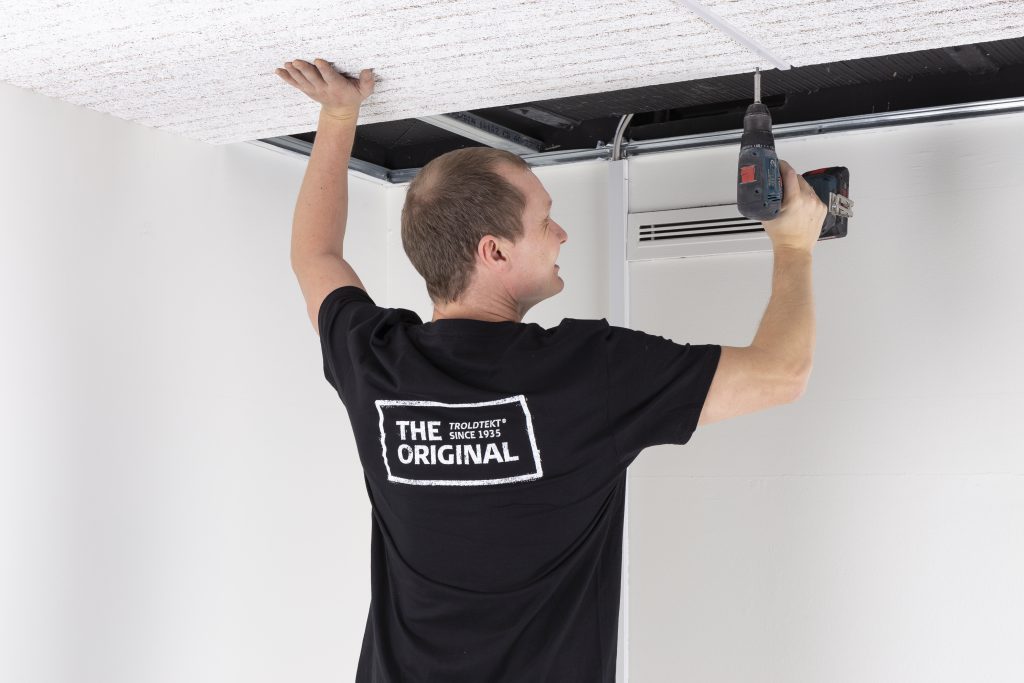 Troldtekt® Employee showing you how Acoustic Panels are Simple to Install and Maintain with his black tshirt and right hand holding a drill, installing an acoustic panel for a customer like you
